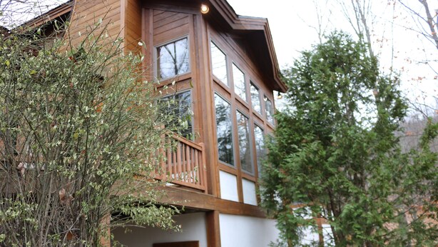 A two-story wooden house with large windows and a balcony.