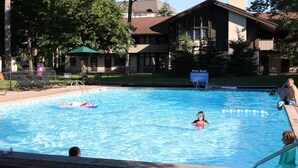 A swimming pool with a pool rule sign, lounge chairs, and a building in the background.