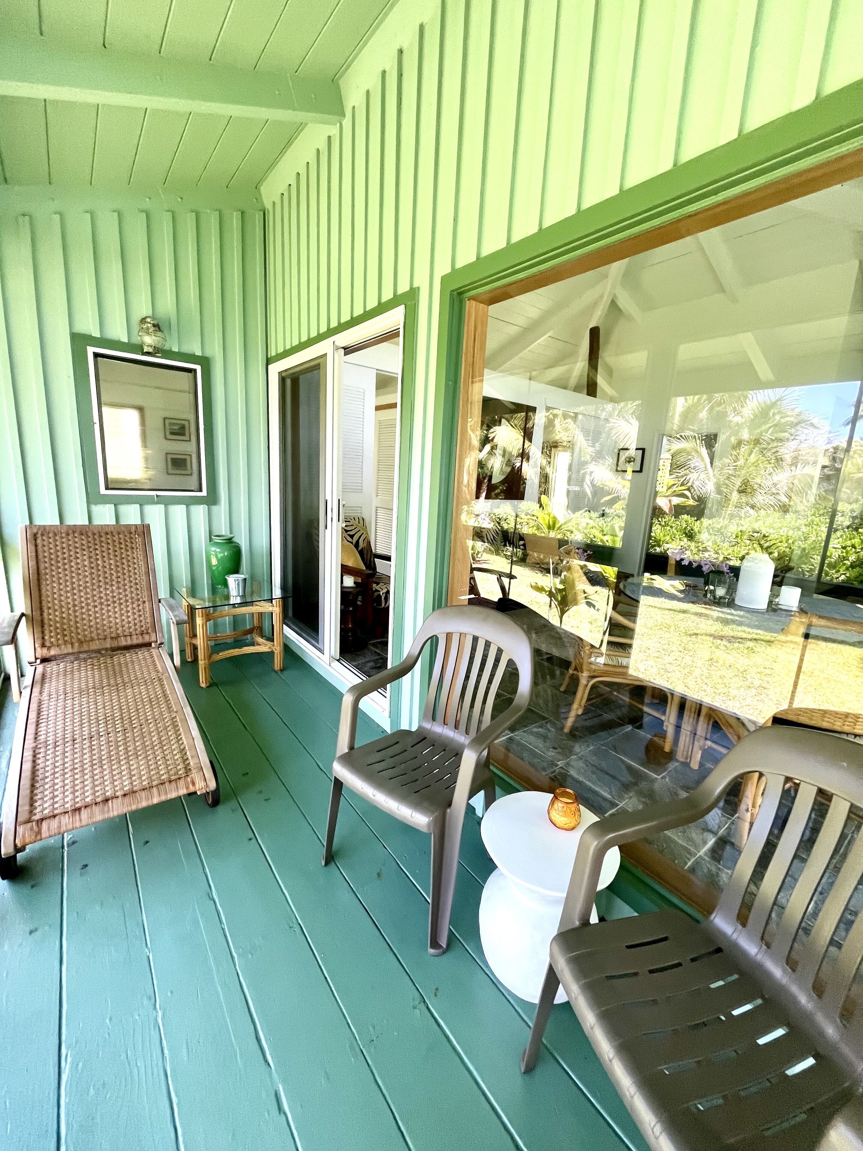 A covered porch with wicker chairs and a table, a sliding glass door, and a view of the garden.