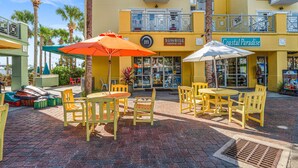 Un área de estar al aire libre con sillas y mesas amarillas, sombrillas y un edificio con un letrero que dice "Sunrise Coffee Co." y "Coastal Paradise".