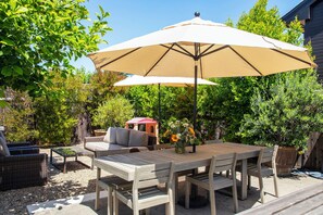 An outdoor patio with a wooden table and chairs, a beige umbrella, wicker furniture, and a potted plant. - Sonoma County Historic Home With Pool; 5 Min Walk to Cyrus, Diavola & Catelli's (Geyserville)