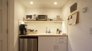 A compact kitchen with a dishwasher, a microwave, a toaster, a sink, and a small countertop with various items.