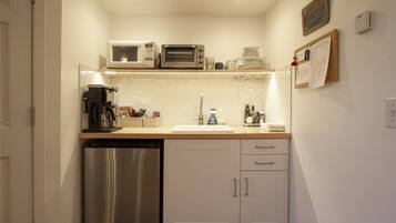 A compact kitchen with a dishwasher, a microwave, a toaster, a sink, and a small countertop with various items.