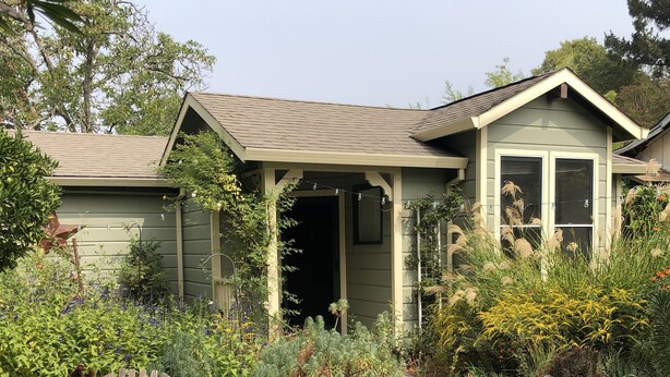 A house with a porch, two wooden chairs with red cushions, and a fire pit.