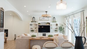 Un salon moderne avec un canapé, une table basse et un téléviseur. On y trouve des étagères ornées d’objets décoratifs et une cheminée.
