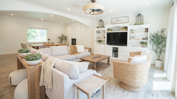 Un salon spacieux avec un grand canapé d’angle, une table basse en bois et un téléviseur fixé au mur.