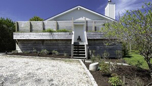 A house with a front porch, a staircase leading to the door, and a small garden area. - PRICE REDUCED Family Friendly, 3Bd Centrally Located Home with Fenced in Yard (Montauk)