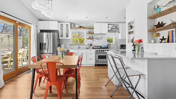 A modern kitchen with white cabinets, a wooden dining table, and orange chairs. - PRICE REDUCED Family Friendly, 3Bd Centrally Located Home with Fenced in Yard (Montauk)