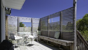 A wooden deck with a table and chairs, a bench with cushions, and a railing. - PRICE REDUCED Family Friendly, 3Bd Centrally Located Home with Fenced in Yard (Montauk)