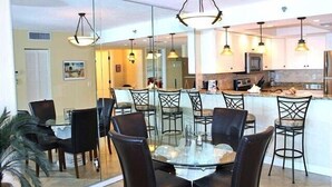 Una cocina moderna con una isla central, una zona de comedor con mesa y sillas de vidrio, e iluminación colgante.