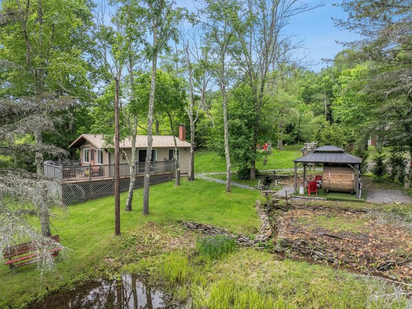 Une cabane avec une terrasse, un petit abri de jardin et un étang.