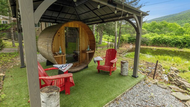 Una estructura de madera con una entrada circular, dos sillas Adirondack rojas, una mesita y una botella de agua.