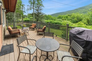 Une terrasse en bois, agrémentée de mobilier d’extérieur, notamment des chaises et une table, qui offre une vue sur un paysage verdoyant et luxuriant.