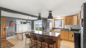 A modern kitchen with a large island, bar stools, wooden cabinets, and a view to the outside. - Cozy cabin with 100 ft of lake shore in the heart of the brainerd lakes area! (Brainerd)