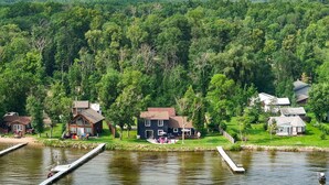 A lakeside property with multiple houses, docked boats, and a grassy area with outdoor seating. - Cozy cabin with 100 ft of lake shore in the heart of the brainerd lakes area! (Brainerd)