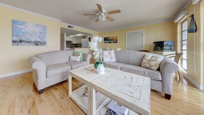 A living room with a ceiling fan, two grey sofas, a coffee table, and a window with blinds. - Wake to the Sunrise and Steps to the Sunset! Best of Both Worlds! (Indian Rocks Beach)