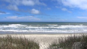 Une plage avec des vagues, un ciel dégagé et des dunes herbeuses.