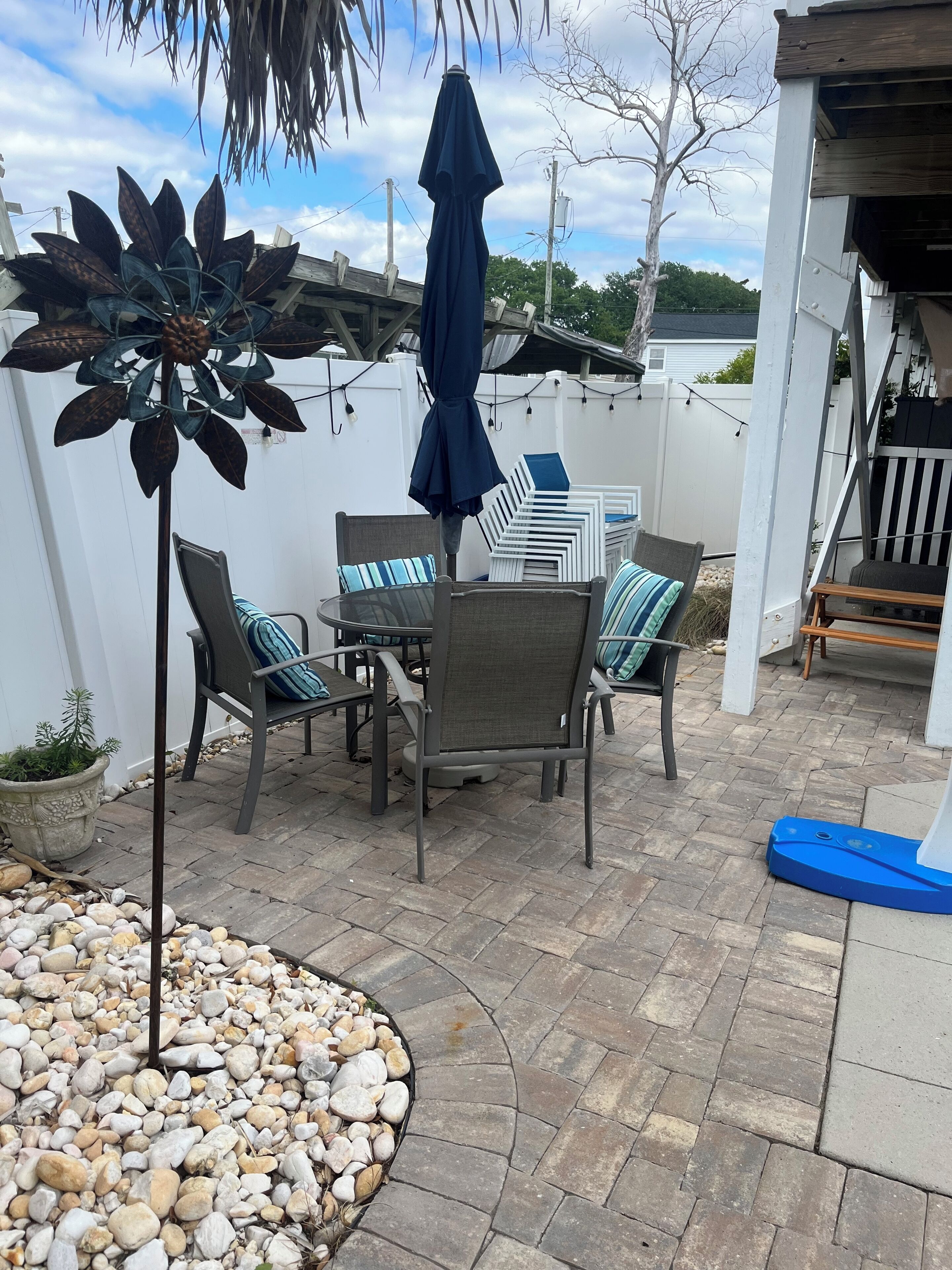 Eine Terrasse im Freien mit Tisch und Stühlen, umgeben von einem weißen Zaun und einem blauen Sonnenschirm.