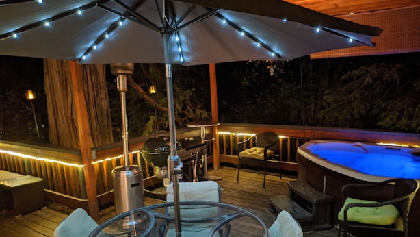 Um deck externo com mesa de vidro, cadeiras, churrasqueira e ofurô.