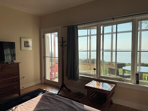 Une chambre avec une grande fenêtre, un lit, une commode et un porte-manteau.