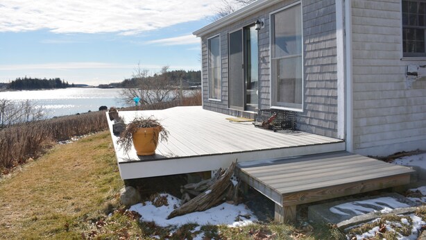 A single-story house with a deck, large windows, and a view of a lake. - Watch the sun rise without getting out of bed! (South Thomaston)