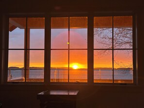 A room with a large window divided into six panes, offering a view of a sunset over a body of water.