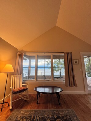 A room with a view of the sea, a table, a chair, and a lamp.