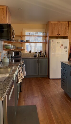 A kitchen with wooden cabinets, a refrigerator, a microwave, and a window above the sink.