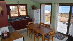 A kitchen with wooden cabinets, a refrigerator, and a dining table with chairs. There is a window with a view of the outdoors. - Watch the sun rise without getting out of bed! (South Thomaston)