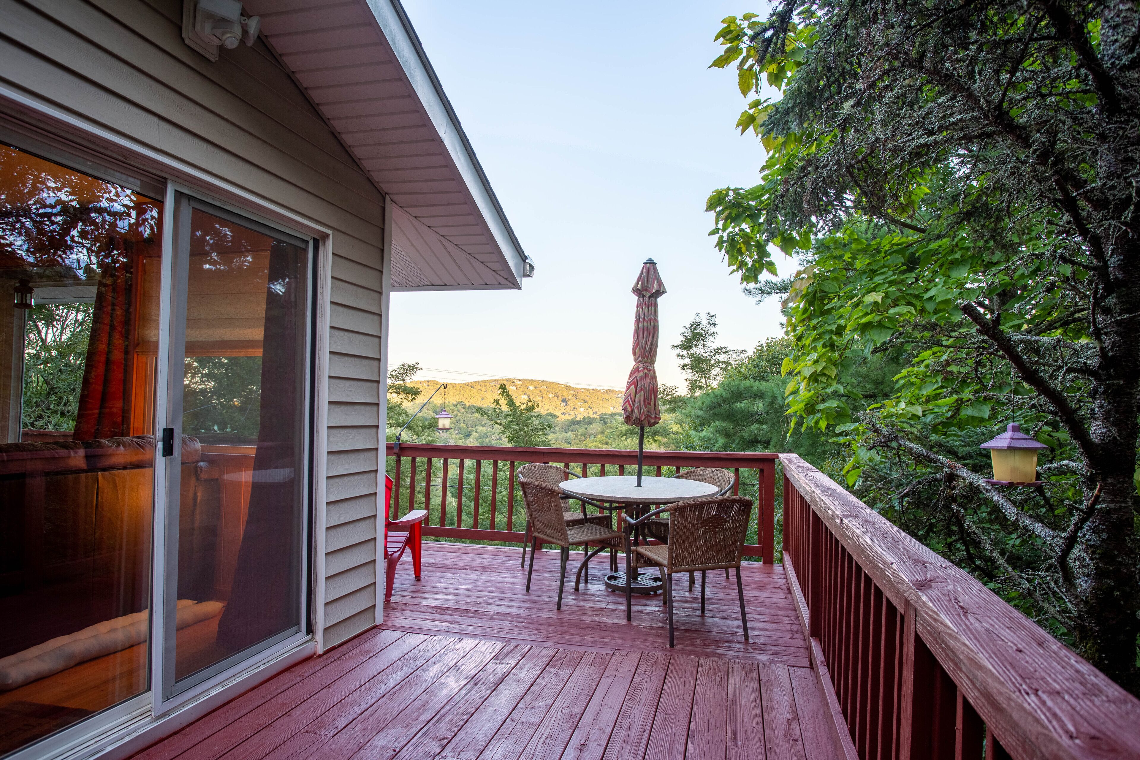 A wooden deck with a table and chairs, a sliding glass door, and a view of a mountain.