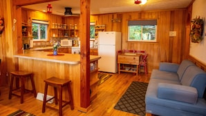 Interior de una cabaña de madera con cocina, comedor y un sofá azul.