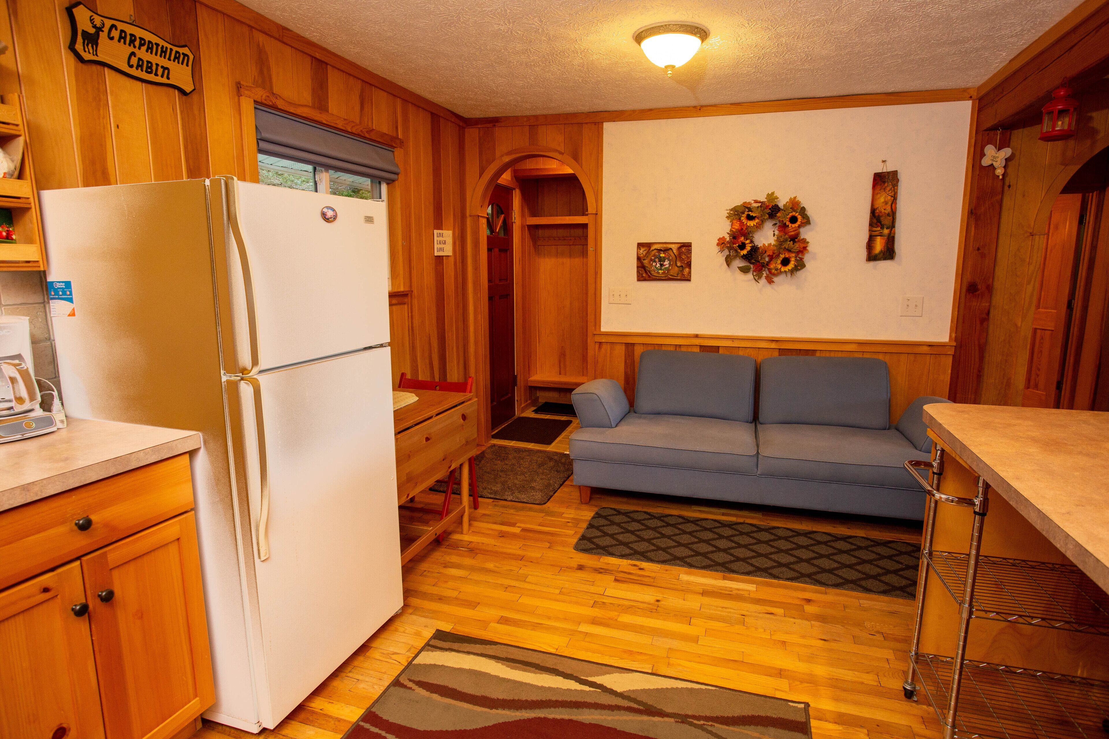 A compact kitchen with wooden cabinetry, a white refrigerator, a blue sofa, and a small dining area.