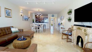 A living room with a brown sofa, a wicker ottoman, a fireplace, and a television mounted on the wall. - 333 Mariners Club - 3 bedroom condo with panoramic ocean views (Key Largo)