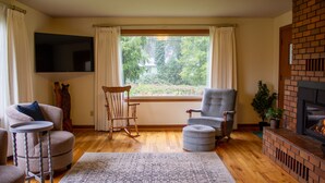 A living room with a fireplace, a television, a rocking chair, and a view of greenery outside.