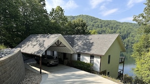 A house with a garage, a driveway, and a view of a lake surrounded by trees. - Nantahala Getaway-Lakefront -mountain views. Firepit,Generator, wifi - STARLINK  (Topton)