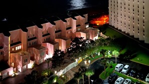 A night view of a coastal hotel with a moonlit sky, a parking area, and a building with a unique architectural design. - 9th Floor Beach Front Condo Tides @ Topsl (Destin)