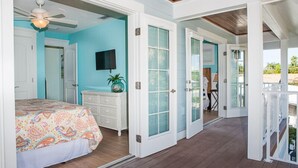 Un dormitorio con cama, cómoda y televisión. Hay puertas que dan a un balcón.