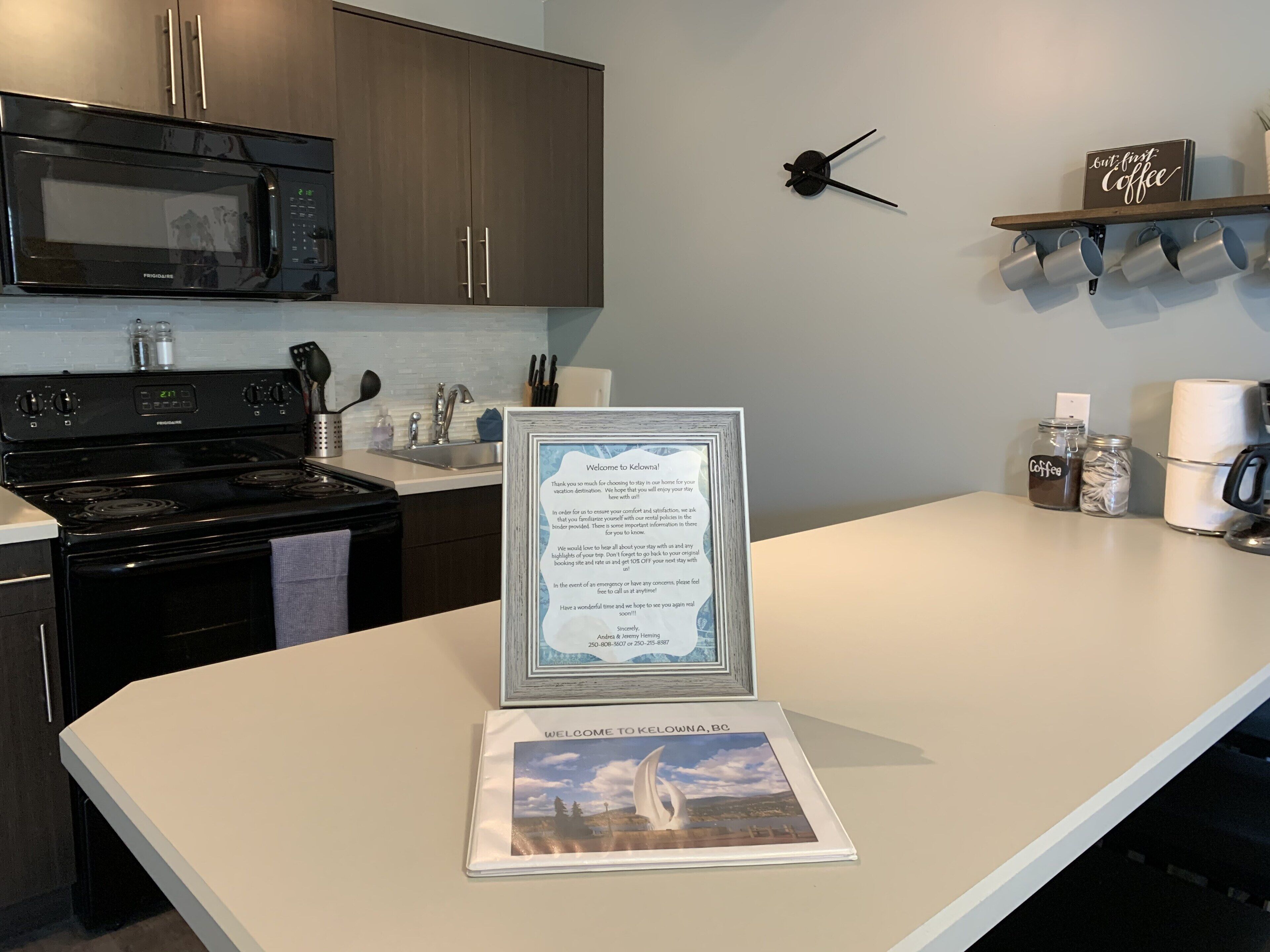 A kitchen with a microwave, stove, and cabinets. There is a welcome sign and a framed welcome to Kelowna sign on the counter.