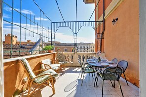 A balcony with wicker chairs and a table set for dining, overlooking a cityscape. - Authentic Roman - Colosseum area, Fabulous Apart, Terrace, Wifi, Aircon (Roma)