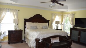 A bedroom with a large bed, a wooden nightstand, a dresser, a television, and a ceiling fan. - Modern 4BR Retreat — Minutes from Mercedes-Benz Stadium - World Cup Ready (Atlanta)