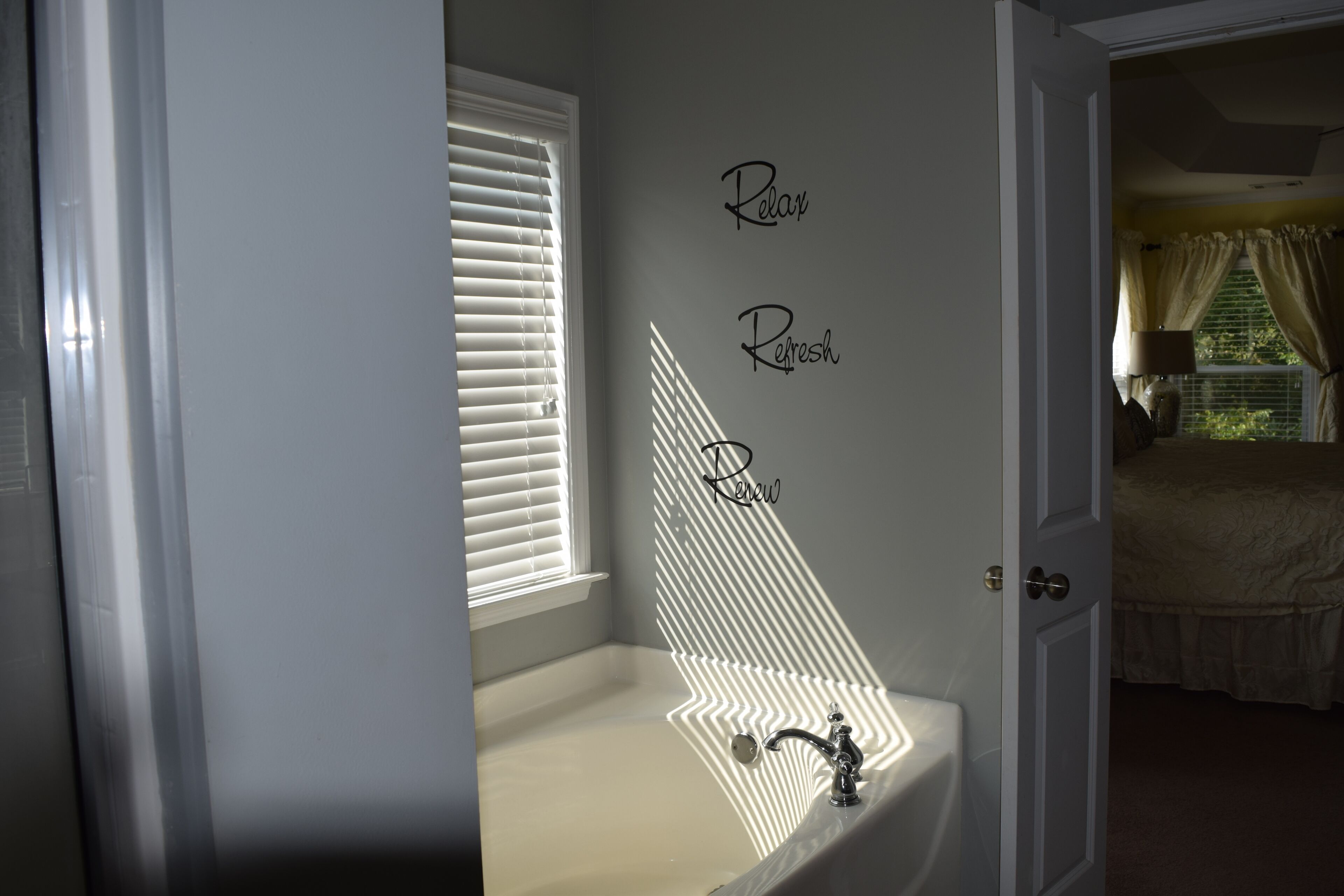 Une salle de bain avec une baignoire, une fenêtre avec des stores et un mur sur lequel sont inscrits les mots «Détendez-vous », «Rafraîchissez-vous » et «Renouvelez-vous ».