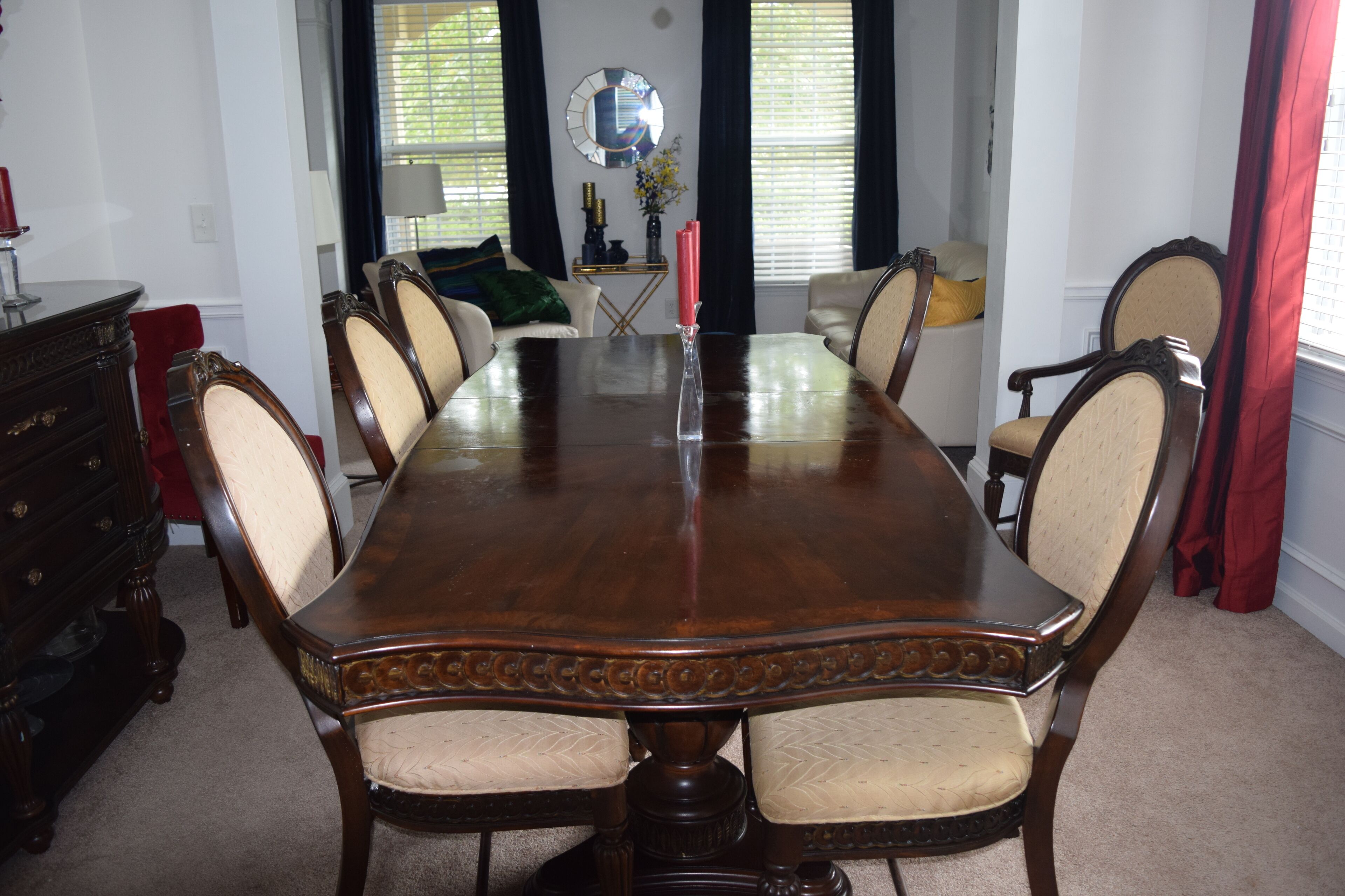 A formal dining room with a large wooden table surrounded by eight chairs, a sideboard, and a mirror on the wall.