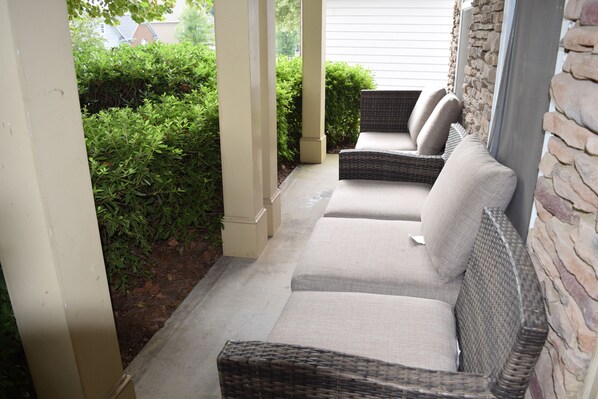 Relax in a secluded outdoor seating area with wicker chairs and benches, surrounded by a well-maintained garden.