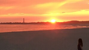 Un atardecer sobre una playa con un faro a lo lejos.