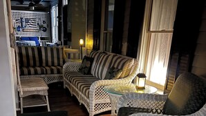 Un espacio interior acogedor con mobiliario de mimbre, incluyendo sofás y sillones, dispuestos alrededor de una mesa de vidrio.