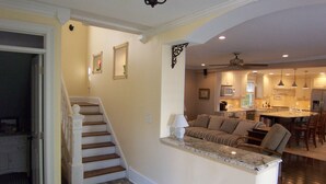 Un interior de hogar con una escalera, una sala de estar con sofá y una cocina con electrodomésticos modernos.