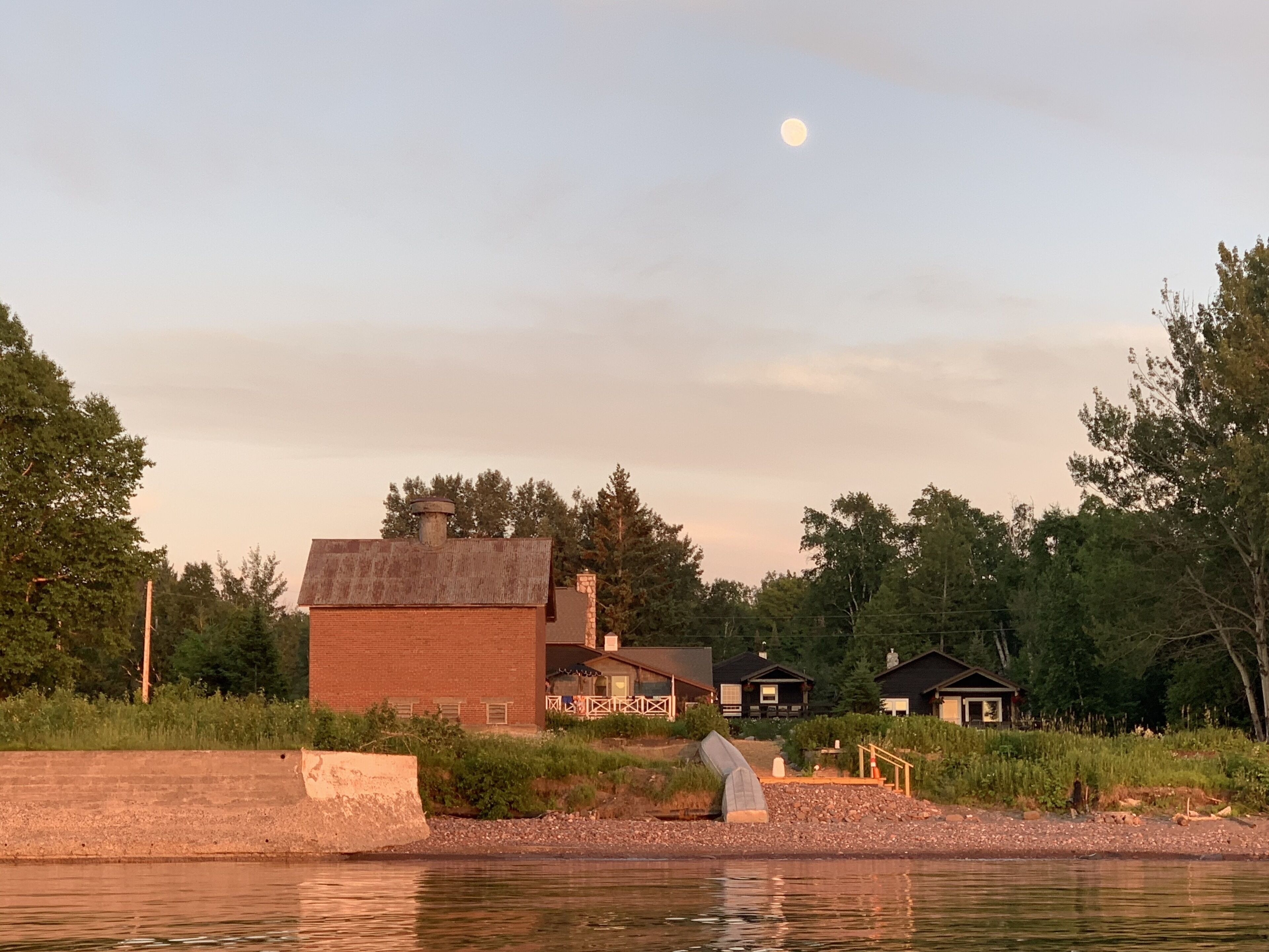 A lakeside cabin with a brick exterior, a chimney, and a small porch.