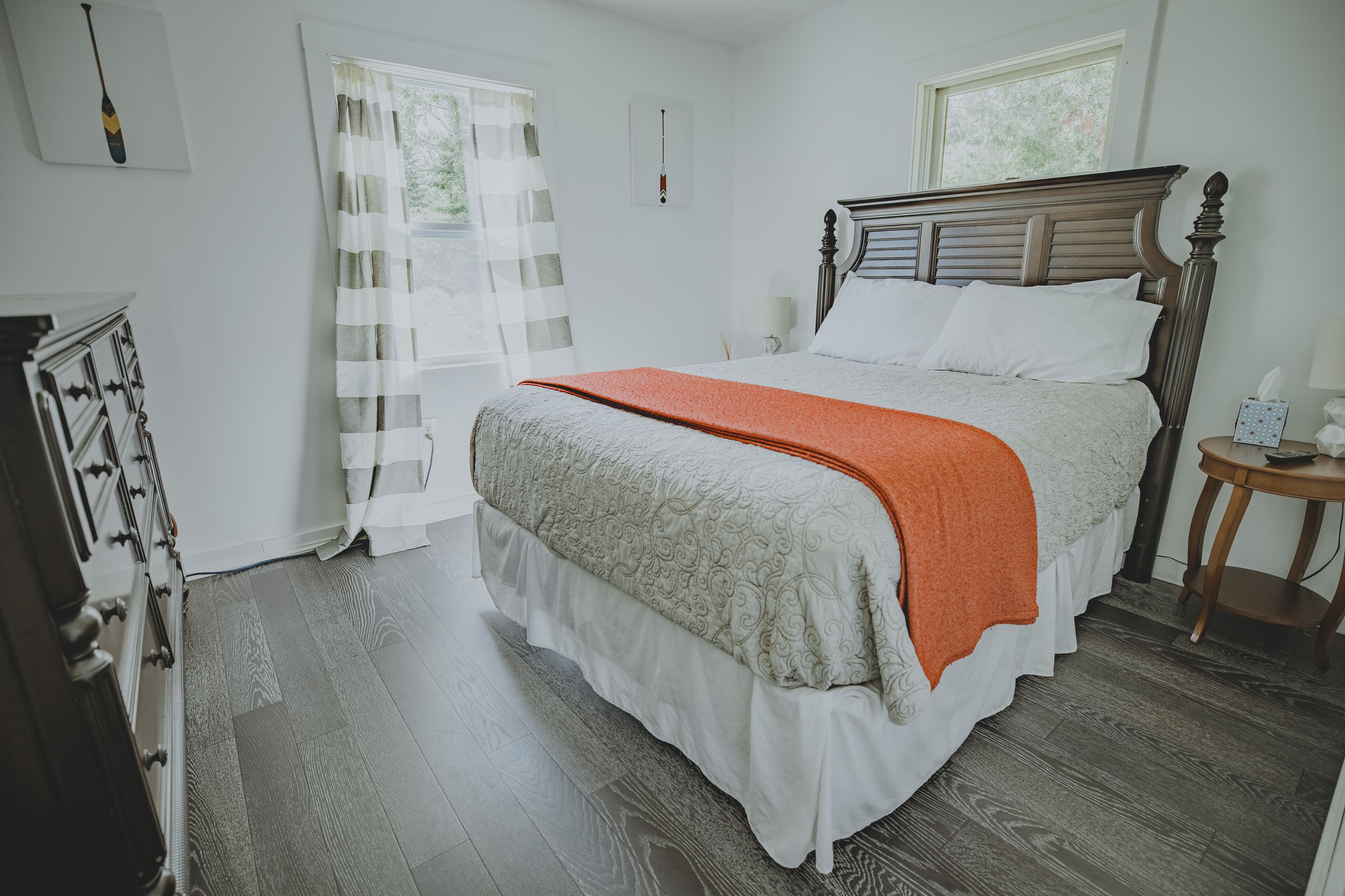 Quarto com cama de madeira, cómoda, mesa de cabeceira e janela com cortinas.