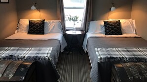 A double room with two beds, each with a pillow, a small table with a vase, and a window with curtains.