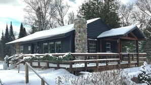A lodge with a stone chimney, wooden deck, and snow-covered surroundings.